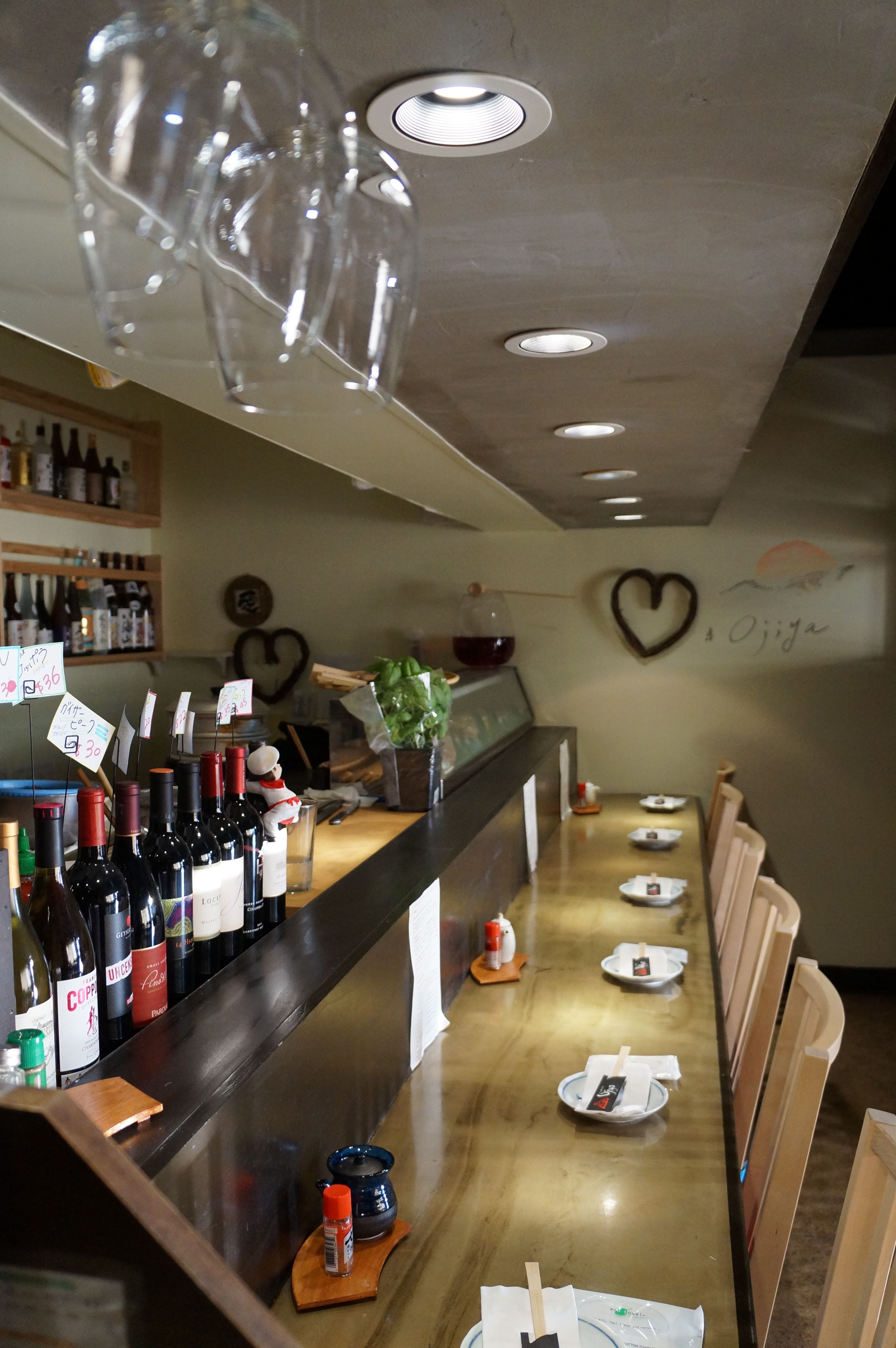 Interior view of Izakaya Ojiya with a wooden bar, empty seats, and a display of sake and wine bottles on the shelf.