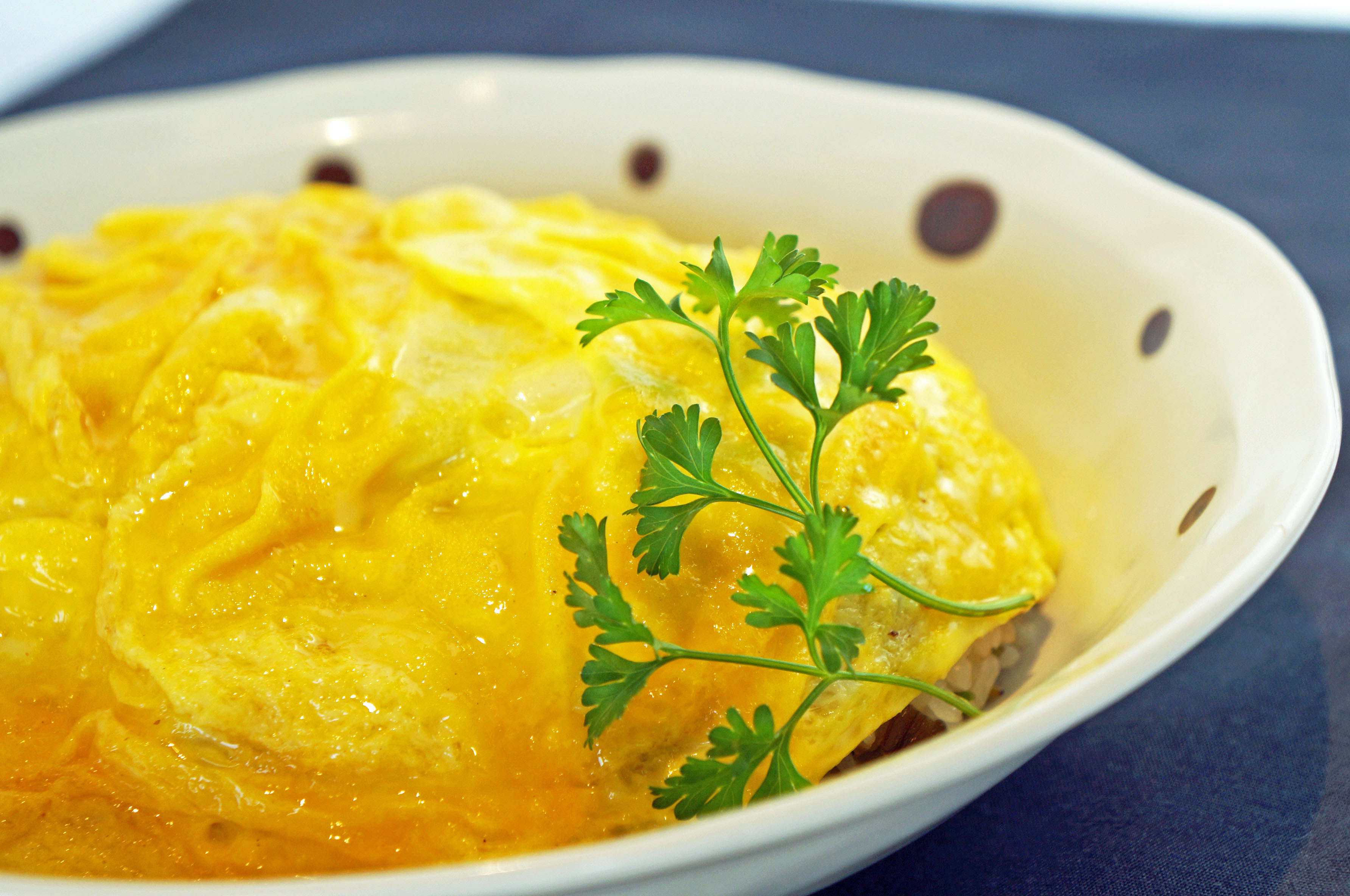 A close-up of a delicious omelette dish, garnished with a sprig of parsley, served in a decorative bowl.